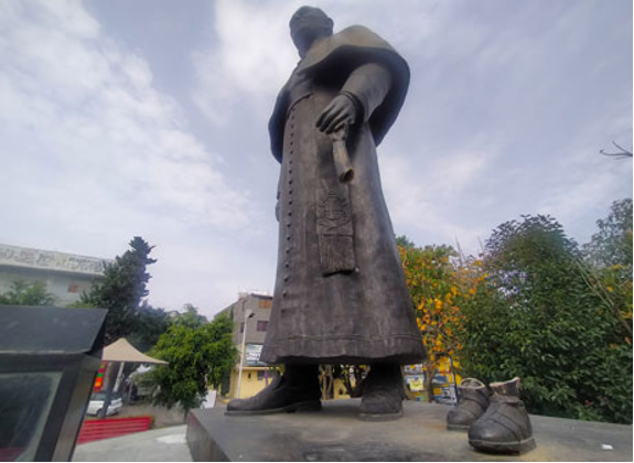 Una estatua de un hombre de pie junto a un par de zapatos.