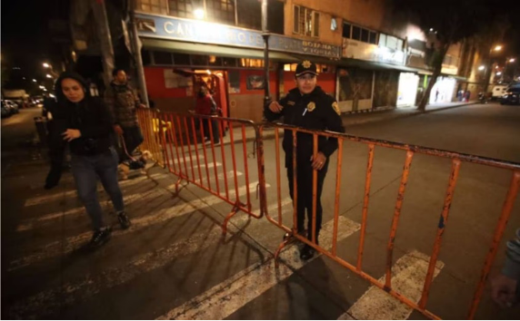 Un oficial de policía está parado frente a una barricada por la noche.