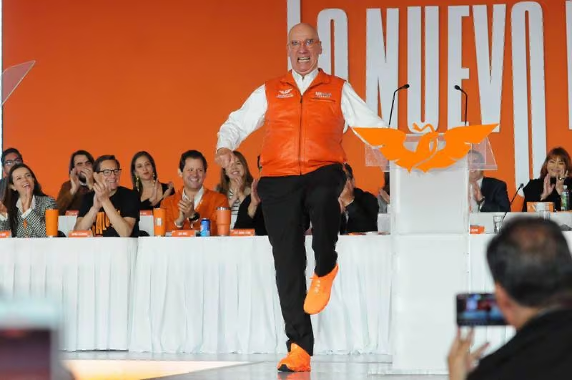 Un hombre con una camisa naranja baila en el escenario frente a una multitud.