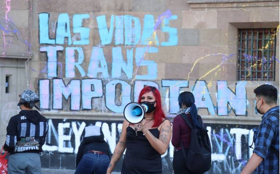 Una mujer sostiene un megáfono frente a una pared con graffiti.