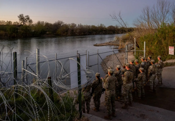 Un grupo de soldados parados cerca de un río con alambre de púas.