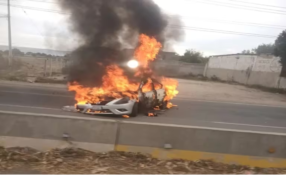 Un auto está en llamas al costado de la carretera.