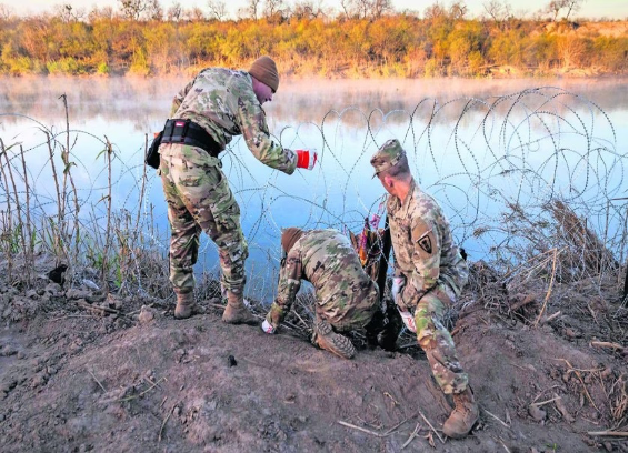 Tres soldados camuflados de pie junto a una masa de agua.