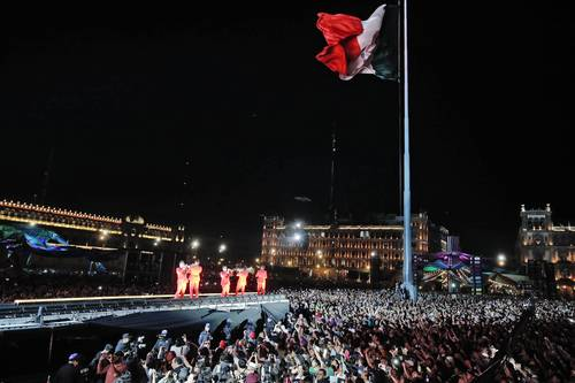 Un gran grupo de personas paradas frente a una bandera mexicana.