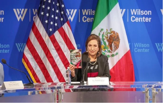 Una mujer sosteniendo un premio frente a una bandera estadounidense y mexicana.