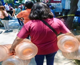 Una mujer con una camisa roja lleva varias vasijas de barro grandes a lo largo de una calle concurrida.