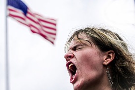 Una persona grita apasionadamente con una bandera estadounidense ondeando de fondo, capturando un momento de intensa expresión.