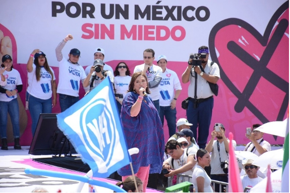 Una mujer habla por un micrófono en una manifestación bajo una pancarta que dice "POR UN MÉXICO SIN MIEDO", rodeada de gente con banderas y cámaras.