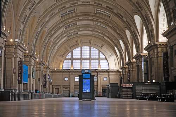 Interior de un gran vestíbulo de estación de tren con altos techos abovedados, grandes ventanales y un quiosco de información en el centro.