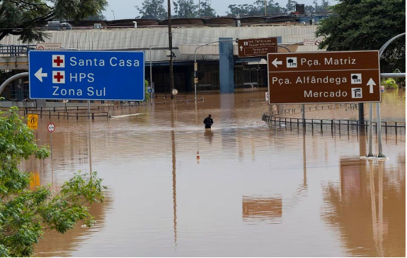 Una persona camina por una calle inundada con señales direccionales y edificios parcialmente sumergidos en el agua.