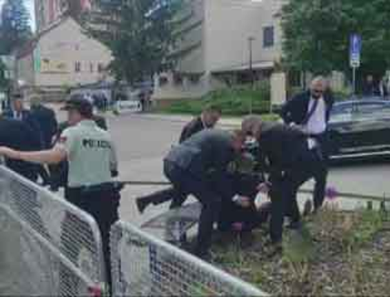 Agentes de policía y varios hombres detiene a un individuo en el suelo cerca de una barricada con curiosos y un coche negro al fondo.