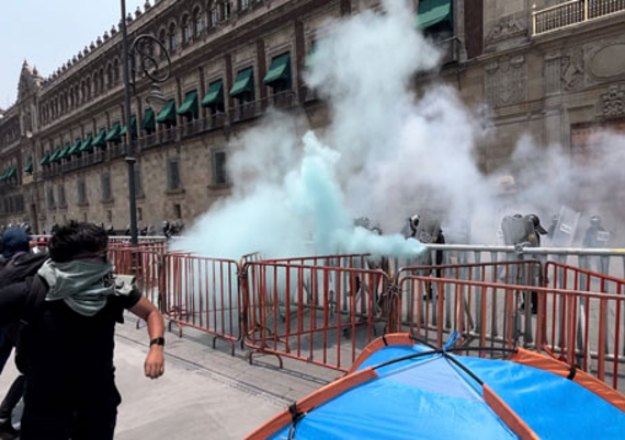 Un manifestante pasa junto a barricadas con humo de un bote de gas lacrimógeno cerca de un edificio gubernamental.