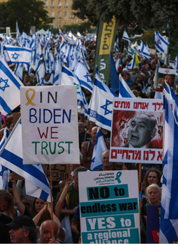 Manifestantes con banderas israelíes y carteles políticos, que incluían "IN BIDEN CONFIAMOS", "NO a la guerra sin fin" y un cartel con la imagen de una persona con texto en hebreo.