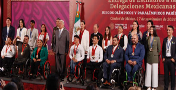 Un grupo de personas, entre ellas atletas en silla de ruedas, se encuentran en el escenario con medallas colgadas del cuello durante un evento en la Ciudad de México. Una pancarta en el fondo hace referencia a los Juegos Olímpicos y Paralímpicos.