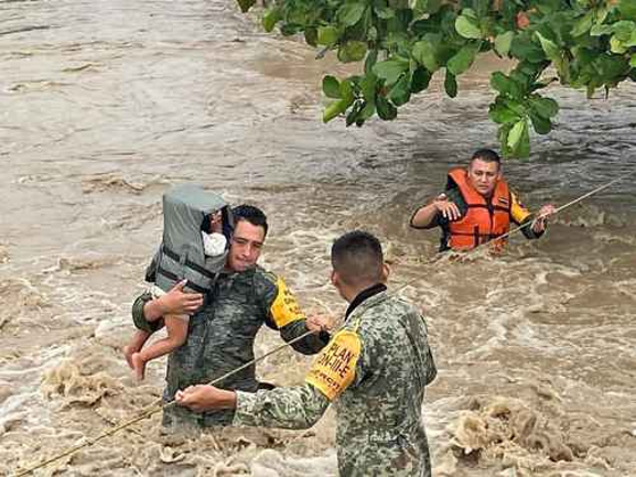 Los equipos de rescate con chalecos salvavidas ayudan a un niño y a otras personas a cruzar un río inundado utilizando cuerdas.