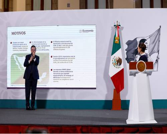 Dos personas dan una presentación en el escenario, una habla en un podio y la otra hace un gesto hacia una gran pantalla que muestra información en español. Una bandera mexicana se interpone entre ellos.