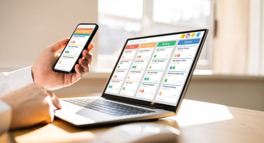 Una persona sostiene un teléfono inteligente que muestra una aplicación de gestión de proyectos y organizar tu vida sin problemas, mientras usa una computadora portátil con una interfaz similar que muestra tareas categorizadas como "En progreso", "Prueba" y "Listo".
