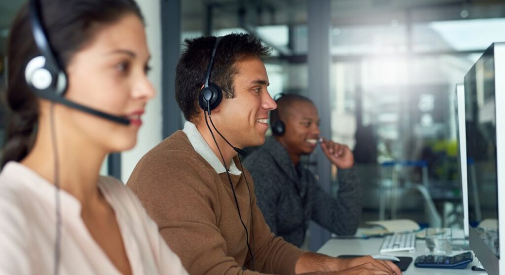 Tres personas con auriculares trabajan frente a computadoras en un entorno de oficina, concentradas en sus pantallas y brindando una atención al cliente excepcional.