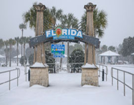 Una puerta de entrada cubierta de nieve dice "Florida le da la bienvenida", con palmeras y nieve de fondo.