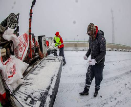 Trabajadores con ropa de invierno esparcen sal en una carretera nevada desde la parte trasera de un camión para evitar la formación de hielo.