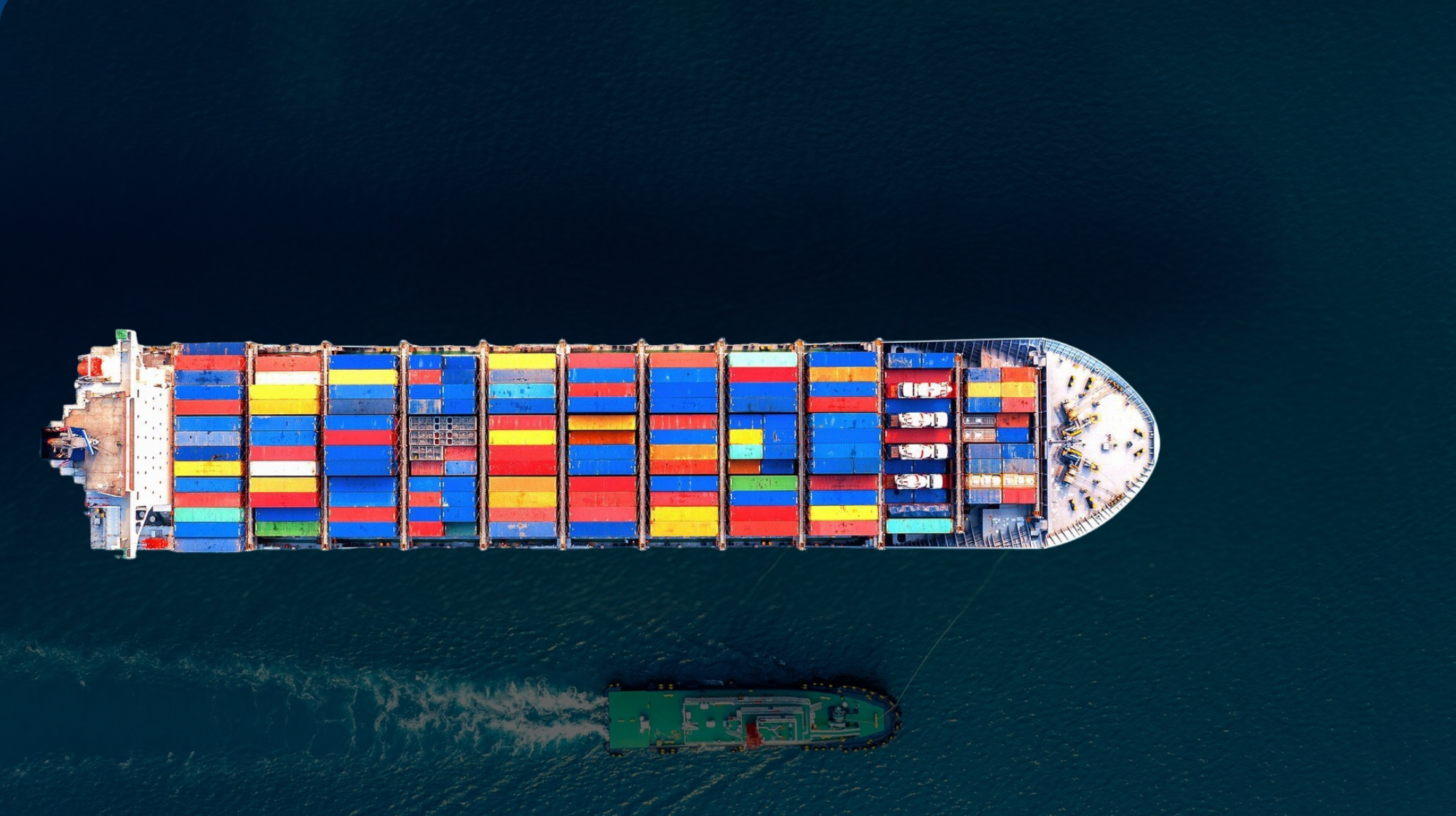 Vista aérea de un gran barco de carga con contenedores coloridos navegando por aguas azules profundas.