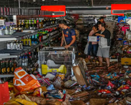 Las personas recorren un pasillo desordenado en una tienda con artÃ­culos dispersos y escombros en el piso. Los estantes estÃ¡n desorganizados y una persona empuja un carrito mientras otras llevan artÃ­culos.
