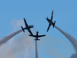 Tres aviones en formación, volando por el cielo con estelas de humo detrás de ellos.