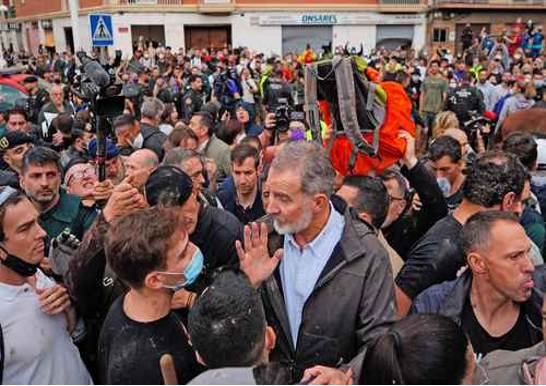 Una gran multitud se reúne al aire libre y algunas personas conversan. Fotógrafos y curiosos se encuentran presentes en la animada escena.
