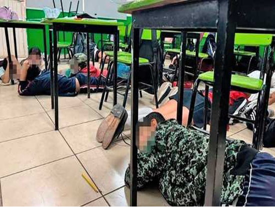 Estudiantes acostados debajo de los escritorios en un aula durante un simulacro de seguridad.