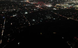 Vista aérea de una ciudad de noche que muestra calles y edificios iluminados con áreas oscuras intercaladas.