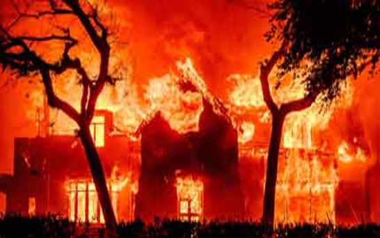 Un gran edificio envuelto en intensas llamas, con una densa columna de humo elevándose hacia el cielo nocturno. Los árboles enmarcan la escena a ambos lados.
