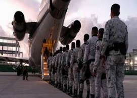 Una fila de personal militar uniformado abordando un avión en una pista durante el anochecer.