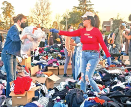 Personas clasificando ropa en un evento de donación al aire libre con cajas y pilas de ropa alrededor. Luz del sol y árboles al fondo.
