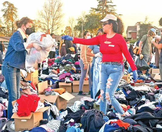 Personas clasificando ropa donada al aire libre, rodeadas de pilas de prendas y cajas de cartón.