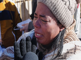Una persona con un gorro de punto y guantes se muestra visiblemente emocionada mientras está de pie al aire libre.