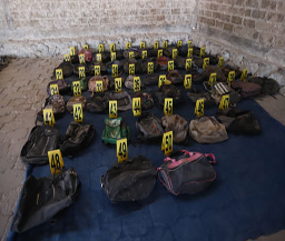 Numerosas bolsas exhibidas sobre una lona azul, cada una marcada con un número de evidencia amarillo, contra un fondo de pared de piedra.