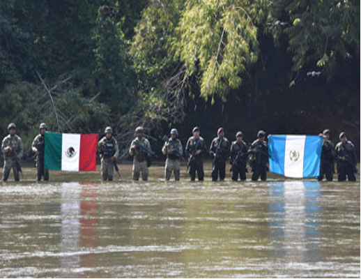 Soldados de pie, con el agua hasta los hombros, sostienen banderas mexicanas y guatemaltecas, rodeados de una densa vegetación.