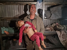 Un hombre, angustiado, sostiene a un niño inconsciente con ropa rosa. Habitación tenuemente iluminada con literas y mantas al fondo.