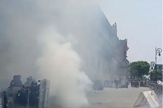 Agentes de policía con equipo antidisturbios detrás de una barricada con humo en primer plano en una calle de la ciudad.
