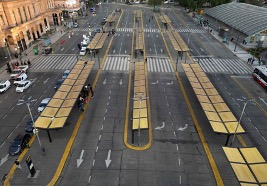 Vista aérea de una intersección de la ciudad con múltiples pasos de peatones y paradas de autobús amarillas, tráfico ligero y algunos peatones.