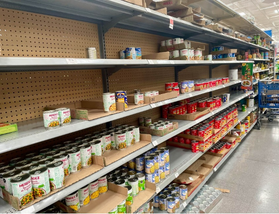 Estantes de supermercado parcialmente abastecidos que muestran diversos alimentos enlatados en envases de metal y cartÃ³n, y algunas Ã¡reas parecen escasamente llenas.