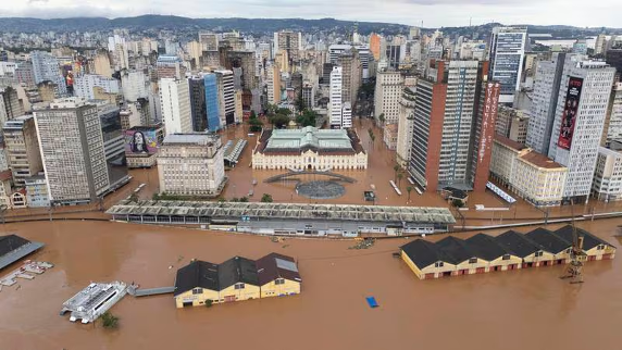 Vista aérea de una zona urbana inundada con edificios sumergidos y aguas turbias que cubren una plaza y calles de la ciudad.