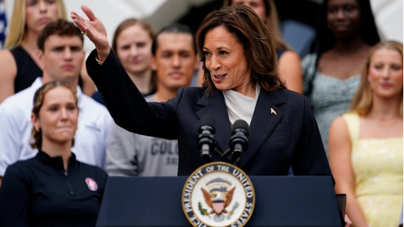 Una mujer habla en un podio con el sello vicepresidencial de Estados Unidos, rodeada de gente detrás de ella.