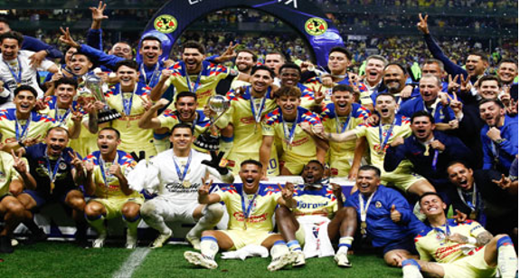 Un equipo de fútbol posa jubiloso para una foto grupal en un campo, sosteniendo un trofeo y luciendo medallas. Los jugadores y el personal visten vestimenta amarilla y azul.