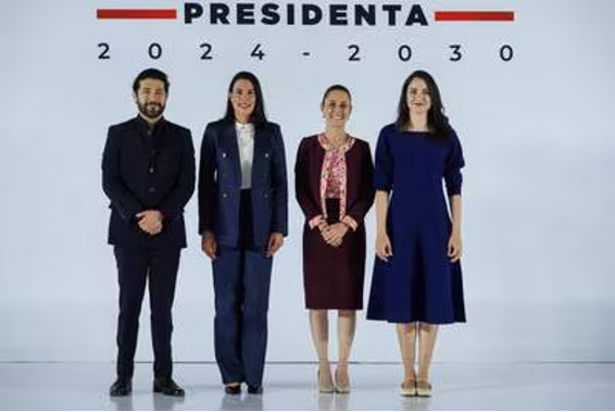 Cuatro personas de pie frente a un fondo con el texto "PRESIDENTA 2024-2030". Las dos personas de la izquierda visten trajes y las dos de la derecha visten vestidos.