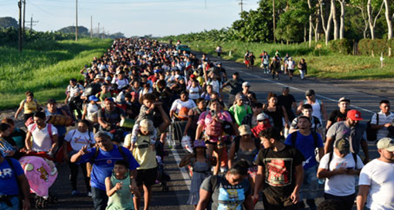 Un nutrido grupo de personas camina por un camino rural, rodeado de vegetaciÃ³n y tendidos elÃ©ctricos, llevando diversas pertenencias.