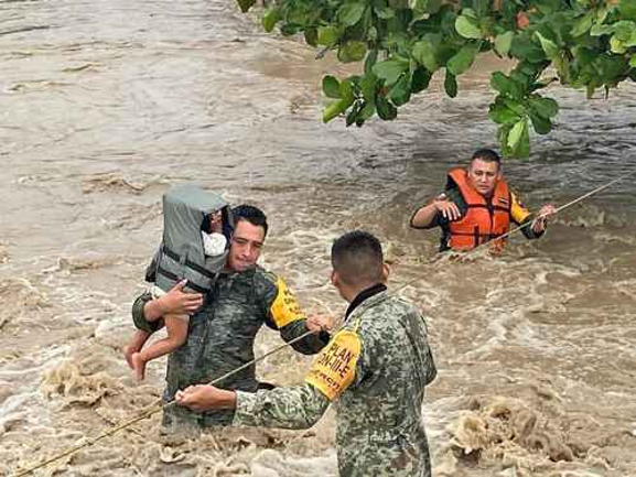 Los equipos de rescate con chalecos salvavidas ayudan a un niÃ±o y a otras personas a cruzar un rÃ­o inundado utilizando cuerdas.