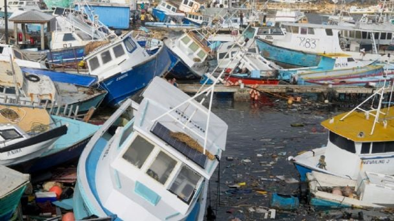 Varios barcos pesqueros están volcados y amontonados en una zona portuaria, con escombros flotando en el agua.