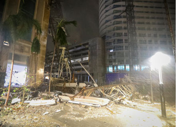 Escombros de edificios derrumbados por la noche, con farolas iluminando las estructuras caídas y los rascacielos circundantes.