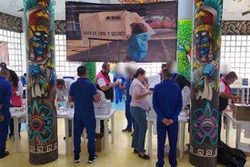 Personas votando en un colegio electoral decorado con pilares coloridos, con una gran pancarta que decía "votar es nuestro derecho".